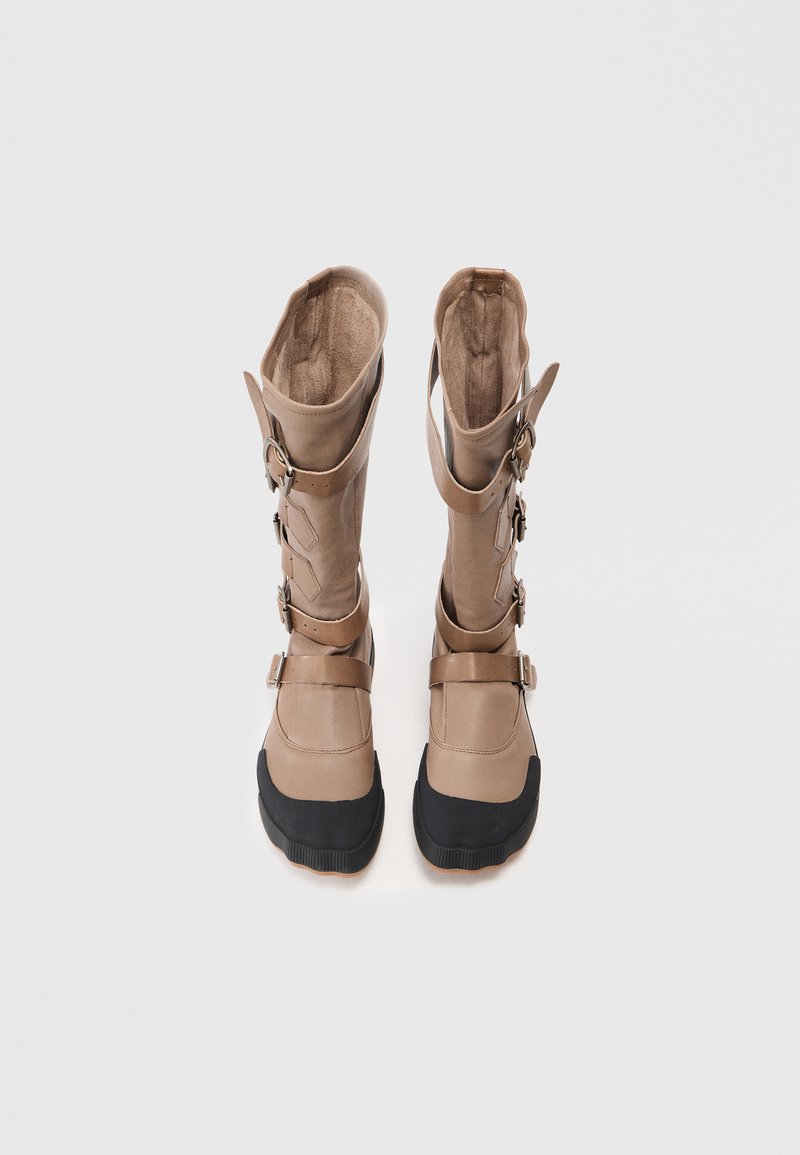 Tan waterproof boots with a high shaft, buckle accents, and a black rubber sole. They feature a smooth surface and a plush inner lining.