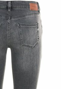 Rückenansicht einer grauen, enganliegenden Denim-Jeans mit rechtem hinteren Taschen und braunem Leder-Logo am Bund.
