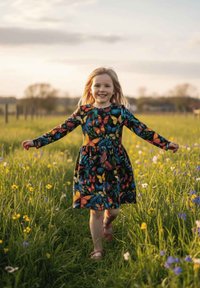 Czarna sukienka w kolorowy wzór motyli, z długimi rękawami i rozkloszowanym dołem. Dziewczyna z długimi włosami spaceruje po polu pełnym kwiatów.