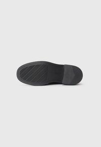 Black shoe sole featuring a textured surface with diagonal grooves, a rounded toe, and a reinforced heel for stability.