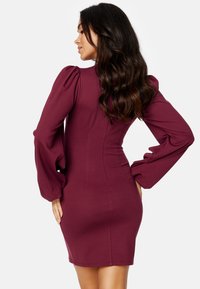 Bordeaux aansluitende jurk met opgeblazen lange mouwen, gemaakt van een gladde stof, met een bodycon ontwerp en subtiele naaddetails.
