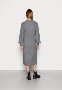 Lungo vestito grigio lavorato a maglia con texture a coste, maniche a palloncino e scollatura rotonda. Abbinato a stivali neri alla caviglia con linguette per il tè.