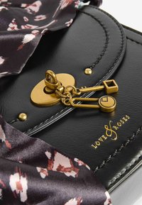 Borsa a tracolla in pelle nera con chiusura in oro e hardware decorativo a forma di chiave. Include una sciarpa in seta a fantasia appesa nella parte superiore.