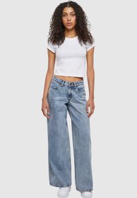 Camiseta blanca corta combinada con jeans de mezclilla de pierna ancha en un tono azul claro. Los jeans tienen un diseño clásico de cinco bolsillos y un lavado desgastado.
