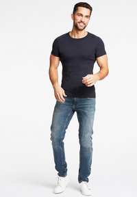 Granatowy t-shirt z krótkim rękawem o dopasowanym kroju, zestawiony z jasnoniebieskimi jeansami slim fit. Model nosi białe sneakersy, stojąc na tle jednolitego tła.