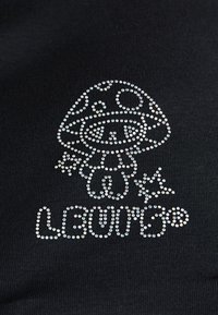Mirdzoši rhinestones veido smaidošu karikatūru sēni, kas tur zvaigzni, ar vārdu "LOUNGE" zemāk uz melnas auduma.