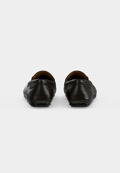 Ζευγάρι μαύρα δερμάτινα loafers χωρίς κορδόνια, εμφανιζόμενα από πίσω σε απλό λευκό φόντο.