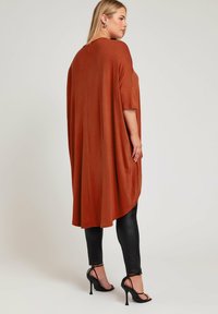 Rostfärgad löst sittande tunika med korta ärmar, tillverkad av mjukt material, i kombination med svarta läderleggings och högklackade sandaler.