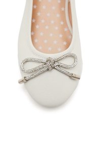 Bailarina blanca con una textura suave, que presenta un detalle de lazo adornado con rhinestones en la punta y una plantilla con patrón de estrellas.