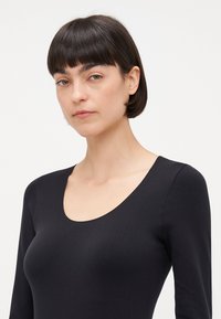 Top noir à manches longues avec un décolleté arrondi, texture lisse, design ajusté et coutures minimales. Uni, sans motifs ni accents visibles.