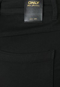 Schwarzer Denim-Stoff mit glatter Textur, der eine sichtbare Tasche und ein Label mit der Aufschrift "ONLY Blue Denim" in goldener Schrift zeigt.