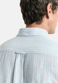Camicia a strisce blu chiaro con colletto, chiusura a bottone al collo e dettaglio a piega sul retro. Realizzata in un morbido tessuto strutturato.