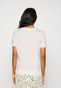 T-shirt branco de manga curta com gola redonda, textura suave e um design simples, usado sobre uma saia estampada de cor clara.