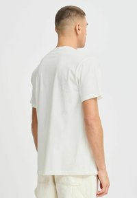 T-shirt à manches courtes de couleur crème clair, fabriqué en coton doux, avec un col rond standard et une coupe décontractée, vu de dos.