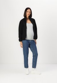 Črna flis bomber jakna z zadrgo, siva majica brez rokavov, modri trijeh jeans in bele superge. Jakna ima elastične manšete in sproščen kroj.