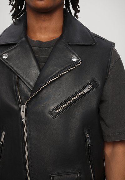 Zwarte leren gilet met een brede kraag, voorrits en meerdere met rits afgesloten zakken. De gladde textuur en het getailleerde ontwerp versterken de structuur.