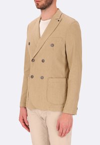 Blazer beige doppiopetto in tessuto strutturato, con due tasche frontali, sei bottoni scuri e rever a punta. Indossato sopra una camicia bianca.