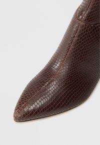 Botine maro, cu varf ascutit, realizate din material texturat cu model de crocodil, avand o finisare lucioasa si detalii de cusaturi vizibile.