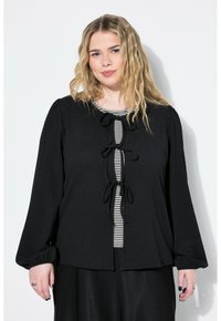Blusa nera con tessitura, maniche lunghe, con un'apertura a chiave decorata con dettagli a righe verticali bianche e nere, legata con fiocchi.