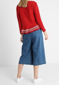 Red ribbed knit sweater with a striped hem, paired with loose blue denim culottes. The outfit is completed with white sneakers.