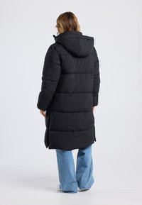 Black puffer coat with a hood, featuring a long design, quilted texture, and side pockets, paired with light blue wide-leg jeans.