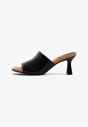 Mule nero con punta aperta, ampio superiore in pelle, soletta imbottita color cuoio e tacco svasato di altezza media su sfondo bianco.