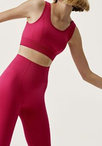 Sujetador deportivo de alto impacto y mallas ajustadas en vibrante magenta. Elaborados con una tela elástica y suave, con un diseño sin costuras y una sutil texturización.