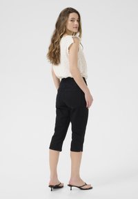 Jeans neri a sigaretta, con un design aderente, vita alta e orlo spaccato. Abbinati a un top chiaro a maniche corte con pois.