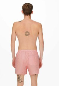 Shorts de bain rayés rouges et blancs avec une taille élastique, dotés d'une poche à l'arrière et d'une finition lisse. Aucuns logos ou graphiques visibles.