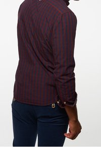 Camisa de manga larga en tartán azul marino y burdeos. Cuenta con puños abotonados, dobladillo curvado y una suave tela de algodón con un ligero brillo.