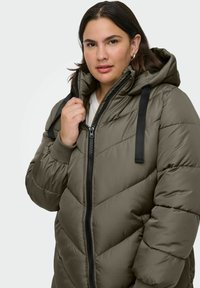 Khaki puffer jacket featuring a hood, zip closure, and black accent straps. The quilted texture adds volume and warmth.