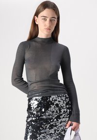 Grå, ribbet langermet topp med høy hals, kombinert med et tettsittende svart paljettbelte, som viser en skinnende, refleksiv tekstur.