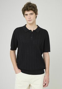 Polo en tricot noir avec une texture côtelée, un col et une patte de boutonnage à trois boutons. Manches courtes avec une coupe décontractée.
