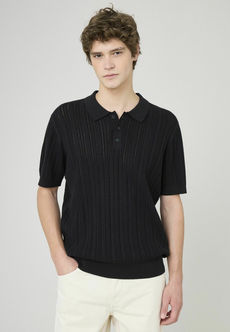 Polo en tricot noir avec une texture côtelée, un col et une patte de boutonnage à trois boutons. Manches courtes avec une coupe décontractée.