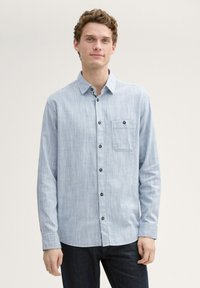 Lichtblauw overhemd met een subtiele gestreepte patroon, een enkele borstzak en donkere knopen, gecombineerd met donkere jeans.