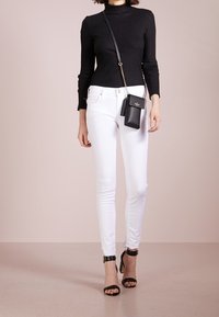 Jersey de cuello alto negro de canalé, jeans ajustados blancos y sandalias de tacón negro con tiras en el tobillo. Incluye un pequeño bolso cruzado negro.