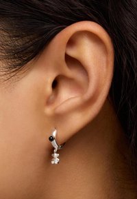 Orecchino a cerchio in argento con una perla nera e accenti simili a perle che pendono in basso. Texture liscia con un design curvo che si complementa con l'orecchio.