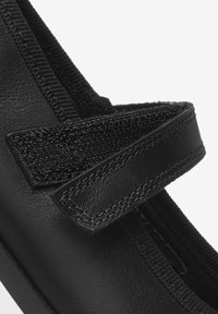 Chaussure noire avec une tige en cuir lisse, une sangle Velcro et des accents en tissu texturé. Détails cousus le long des coutures.