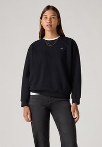 Μαύρο φούτερ με στρογγυλή λαιμόκοψη και μακριά μανίκια, με μικρό λογότυπο Levi's. Συνδυασμένο με σκούρο τζιν, που αναδεικνύει ένα καθημερινό σχέδιο.