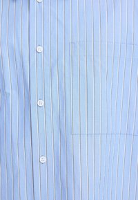 Chemise bleu clair à rayures verticales en coton, avec des boutons blancs, une poche plaquée et des lignes contrastantes discrètes le long des rayures.