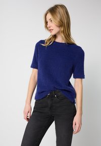Mørkeblå, løs pasform kortærmet sweater lavet af blødt, fuzzy materiale med rund halsudskæring og opkrøllede ærmesøm. Parret med sorte jeans.