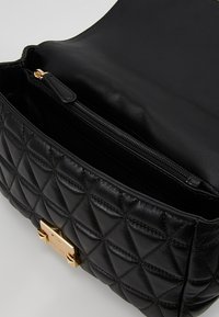 Černá kožená kabelka s prošívaným vzorem, se zlatým kováním a vnitřní kapsou na zip, s hladkou texturou a elegantním designem.