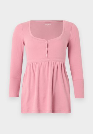 Ροζ μακρυμάνικη ριμπ μπλούζα με τετράγωνο λαιμόκοψη, τρία κουμπιά στο στήθος και λεπτομέρεια με σούρες στη μέση.