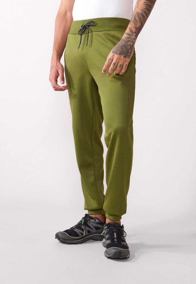 Pantalones jogger verde oliva con cintura elástica y cordón negro, con una textura suave y un diseño ajustado. Llevados con zapatillas gris-negras.