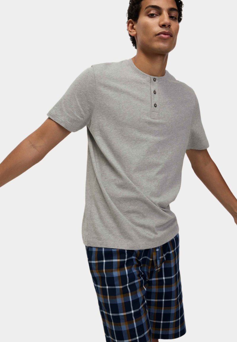 Graues kurzärmliges Henley-Shirt mit einer Knopfleiste aus drei Knöpfen, kombiniert mit Shorts in blau-braunem Karomuster. Weiches Baumwollmaterial mit lockerer Passform.