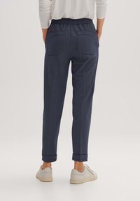 Mörkblå joggingbyxor i strukturerad tyg, med elastisk midja och två bakfickor. Upprullade muddar och bärs med vita sneakers.