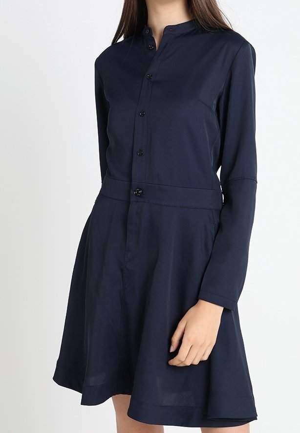 Femme portant une robe bleu marine à manches longues, boutonnée sur le devant, avec un col mao et une jupe évasée.