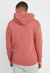 Red sweatshirt with a large hood, soft textured fabric, and ribbed cuffs and hem. Back view shows a relaxed fit with no visible logos.