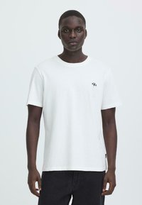 Witte katoenen t-shirt met een ronde halslijn en korte mouwen, met een klein marineblauw paraplu-logo op de linkerkant van de borst.