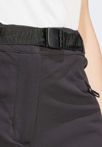 Mustat suorituskykyhousut, joissa on kuvioitu vyö muovisoljella, sivuvetoketjutasku ja sileä kangaspinta.